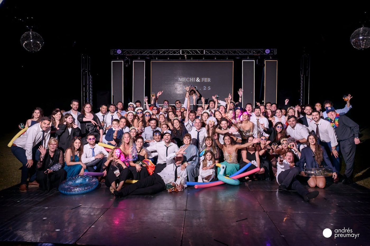 Foto final de todos los invitados de la boda sobre la pista, con la pantalla MECHI y FER de fondo