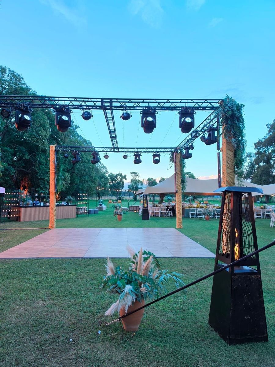 Pista de baile al aire libre bajo una estructura de truss con cabezas m&oacute;viles al atardecer